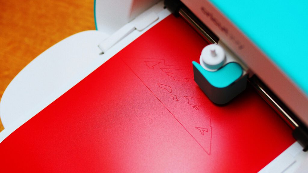 Close-up of a cutting machine engraving a pattern on red paper indoors.