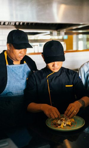 Three chefs collaborate in a kitchen, focused on food preparation and culinary craft.