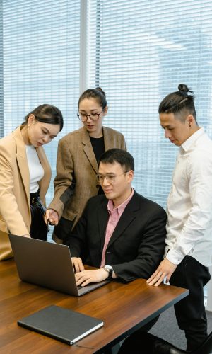 A diverse team collaborates around a laptop in a modern office setting.